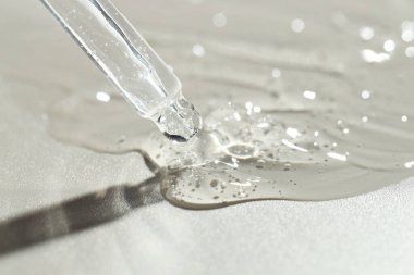 Gri arkaplandaki pipetten kozmetik serumu damlıyor, yakın plan.