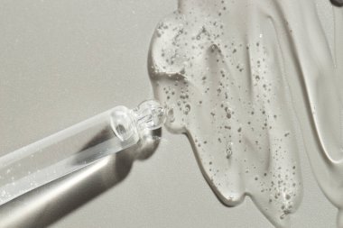 Gri arkaplandaki pipetten akan kozmetik serumu, üst görünüm