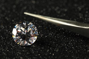 Beautiful dazzling diamond and tweezers on dark shiny background, closeup clipart