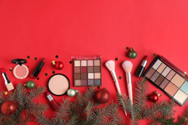 Kırmızı zemin üzerinde makyaj ürünleri ve Noel dekoru olan düz konum, metin için boşluk