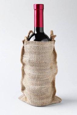 Açık gri arka planda çuval bezi içinde şarap şişesi