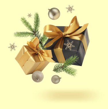 Hediye kutuları, Noel baloları, köknar ağacı dalları ve açık sarı arka planda havada dekoratif kar taneleri.