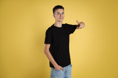 Sarı arka planda siyah tişört giyen genç çocuk.