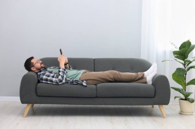 Akıllı telefonlu gülümseyen adam evdeki kanepede dinleniyor.