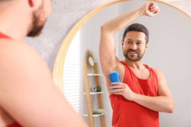 Gülümseyen adam evde aynanın yanında katı deodorant sürüyor.