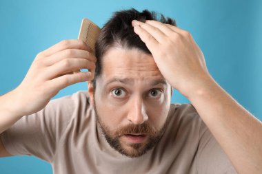 Adam açık mavi arka planda saçını tarıyor. Alopecia sorunu