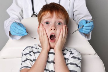 Dental phobia. Dentist working with scared little boy on grey background clipart