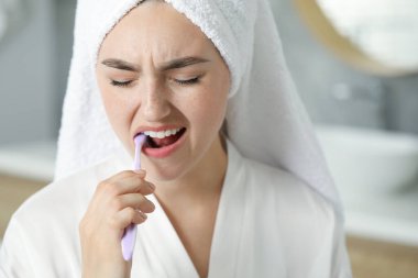 Diş fırçasıyla banyoda diş ağrısı çeken genç bir kadın.
