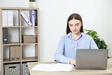 Bütçe planlaması. Ofisteki ahşap masada evrakları ve laptopuyla güzel bir genç kadın.