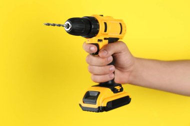 Sarı arka planda kablosuz matkabı olan adam, yakın plan.