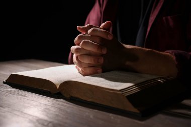 İncilli bir adam ahşap masada dua ediyor, yakın plan.