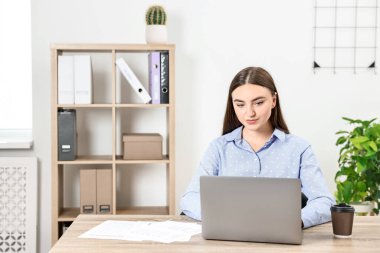 Bütçe planlaması. Ofisteki ahşap masada evrakları ve laptopuyla güzel bir genç kadın.