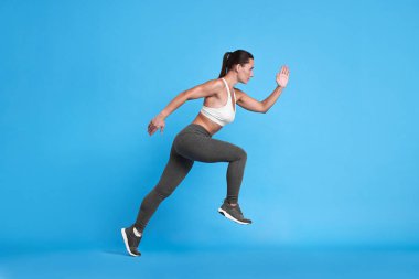 Açık mavi arka planda koşan spor kıyafetli kadın.