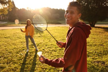 Genç adam ve kadın güneşli bir günde parkta badminton oynuyorlar.