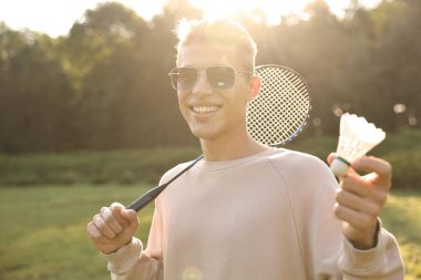 Güneşli bir günde parkta badminton raketi ve pipisi olan mutlu genç bir adam.