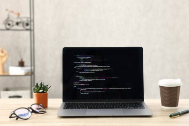 Programcının işyeri. Tamamlanmamış kodu olan modern bir bilgisayar, kağıt bardak, bardak ve ev bitkisi.