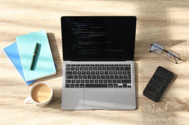 Programcının işyeri. Tamamlanmamış kodu, akıllı telefonu ve ahşap masasında diğer malzemeleri olan modern bir dizüstü bilgisayar.