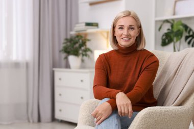 Evdeki koltukta gülümseyen orta yaşlı kadın portresi. Metin için boşluk