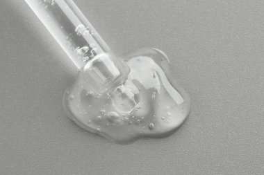 Gri arkaplandaki pipetten akan kozmetik serumu, üst görünüm