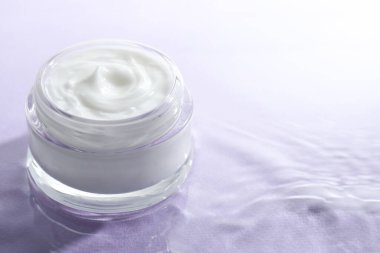 Açık mor arkaplanda suda yüz kremi olan kavanoz, metin için boşluk