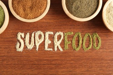 Superfood kelimesi ve ahşap masa üzerindeki farklı sağlıklı tozlar.