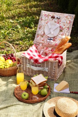 Masa takımlı piknik sepeti, farklı atıştırmalıklar, meyve suyu ve şapka.