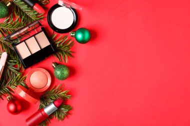 Kırmızı zemin üzerinde makyaj ürünleri ve Noel dekoru olan düz konum, metin için boşluk