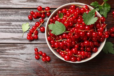 Kasede taze kırmızı frenk üzümü ve ahşap masada yeşil yapraklar.