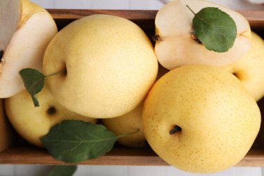 Delicious fresh apple pears in wooden crate and green leaves on table, top view clipart