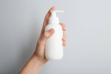 Gri arka planda şampuan şişesi olan kadın, yakın plan.