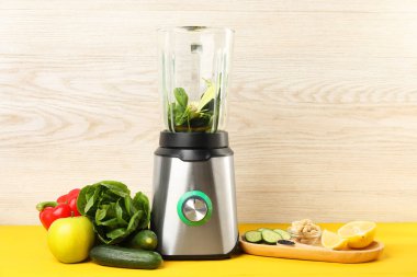 Sarı ahşap masada smoothie için malzeme içeren modern blender.