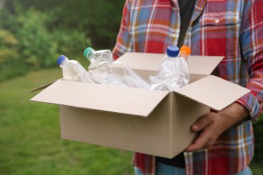 Geri dönüşüm. Elinde plastik şişelerle karton kutu tutan adam, yakın plan.