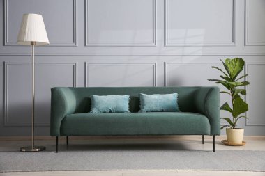 Gri duvarın yanında rahat bir kanepe, çiçek ve lamba.