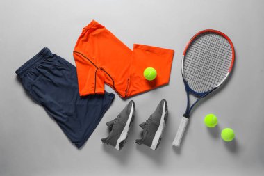 Tenis raketi, toplar, spor ayakkabısı ve gri arka planda spor giysisi, düz yatış