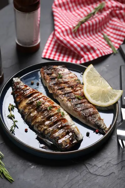 Lezzetli ızgara uskumru, biberiye ve limon tabağı koyu dokulu masada servis edilir.