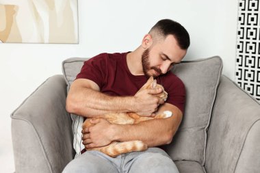 Evdeki koltukta sevimli kızıl kediyi okşayan adam.