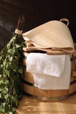 Sauna ekipmanları. Kova, keçeli yün şapka, huş ağacı çırpısı ve havluyla bambu bankta kapalı.
