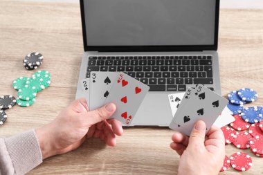 Çevrimiçi poker. Tahta masada kart, fiş ve dizüstü bilgisayarı olan adam, yakın plan.