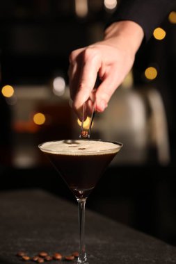 Barmen bardağa kahve çekirdeği koyuyor koyu renkli masada nefis espresso martini ile bulanık ışıklara karşı, yakın plan.