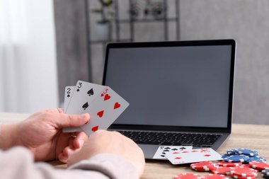 Çevrimiçi poker. Oyun kartları, cipsleri ve laptopu olan adam ahşap masada, yakın plan.
