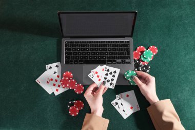 Çevrimiçi poker. Yeşil masada elinde kart ve fiş tutan bir kadın, dizüstü bilgisayarlı, üst görüşlü.