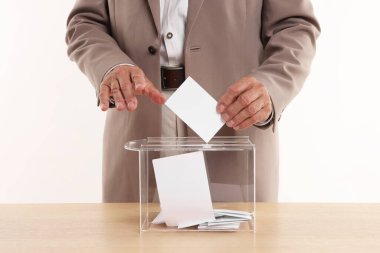 Referandum. Tahta masada, beyaz arka plana karşı oy sandığına koyan adam, yakın plan.