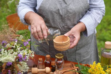 Senior woman making tincture at table outdoors, closeup clipart