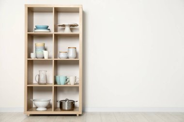 Beyaz duvarın yanında mutfak gereçleri olan ahşap raf ünitesi.