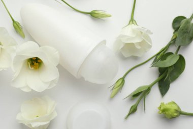 Beyaz arka planda rulo deodorant ve güzel Eustoma çiçekleri, düz yatıyordu.