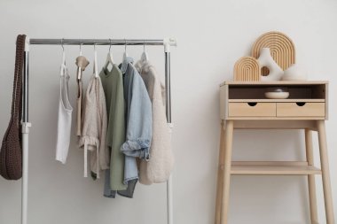 Giysilerle dizilin ve beyaz duvarın yanında ayakta durun.