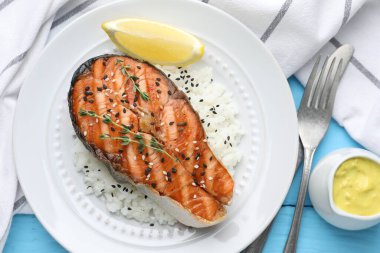 Lezzetli ızgara somon bifteği, pilav, kekik, limon ve susam tohumları açık mavi ahşap masa üzerinde servis edilir.