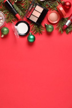 Kırmızı zemin üzerinde makyaj ürünleri ve Noel dekoru olan düz konum, metin için boşluk