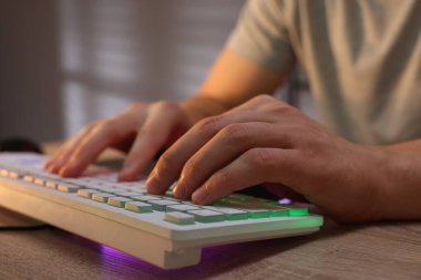 Ahşap masada bilgisayar klavyesi kullanan genç adam, yakın plan.