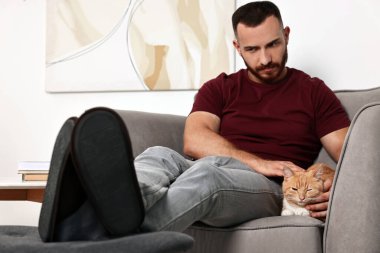 Evdeki koltukta sevimli kızıl kediyi okşayan adam.